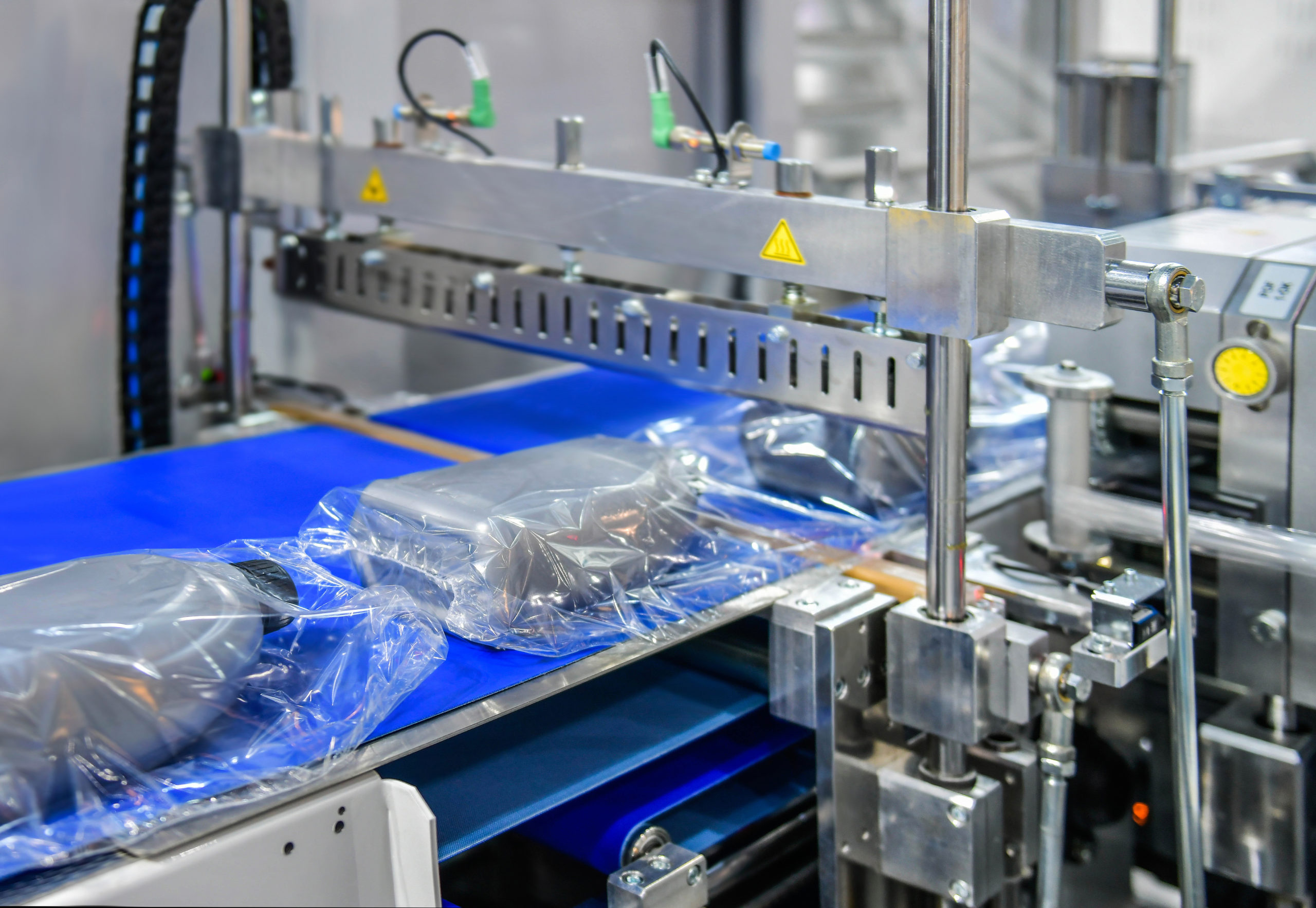 A factory assembly line with machinery is wrapping bottles in plastic packaging.