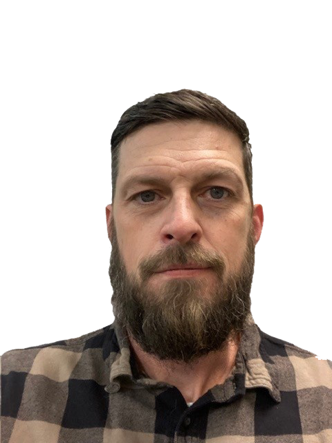 A bearded man with short hair wears a checkered shirt against a plain background.