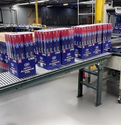A conveyor belt carries multiple cases of Budweiser beer in a warehouse setting.
