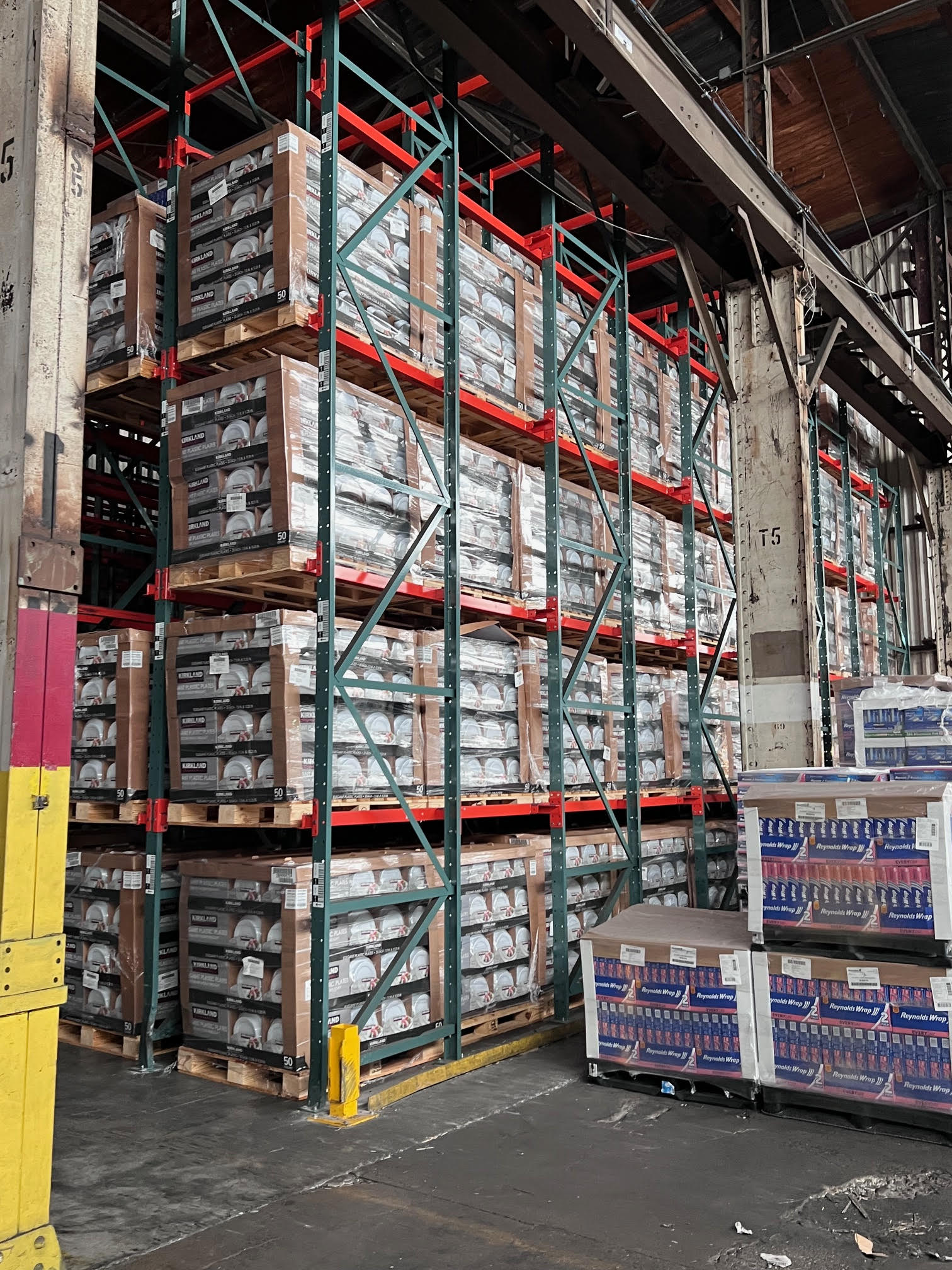 Stacks of pallets with boxes are organized on high metal shelves in a warehouse.