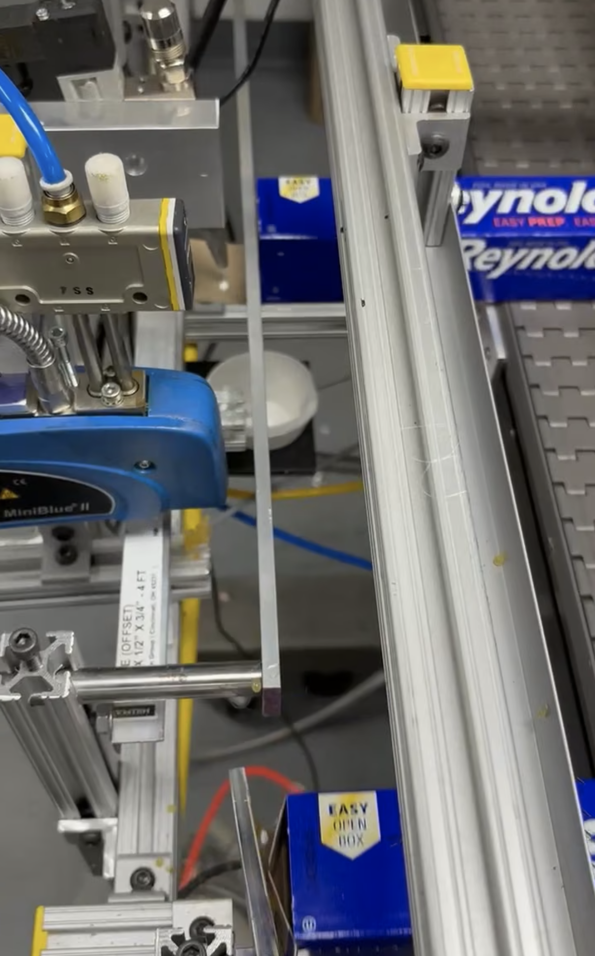A manufacturing machine operates with a moving conveyor belt, and a small item is being processed repeatedly.