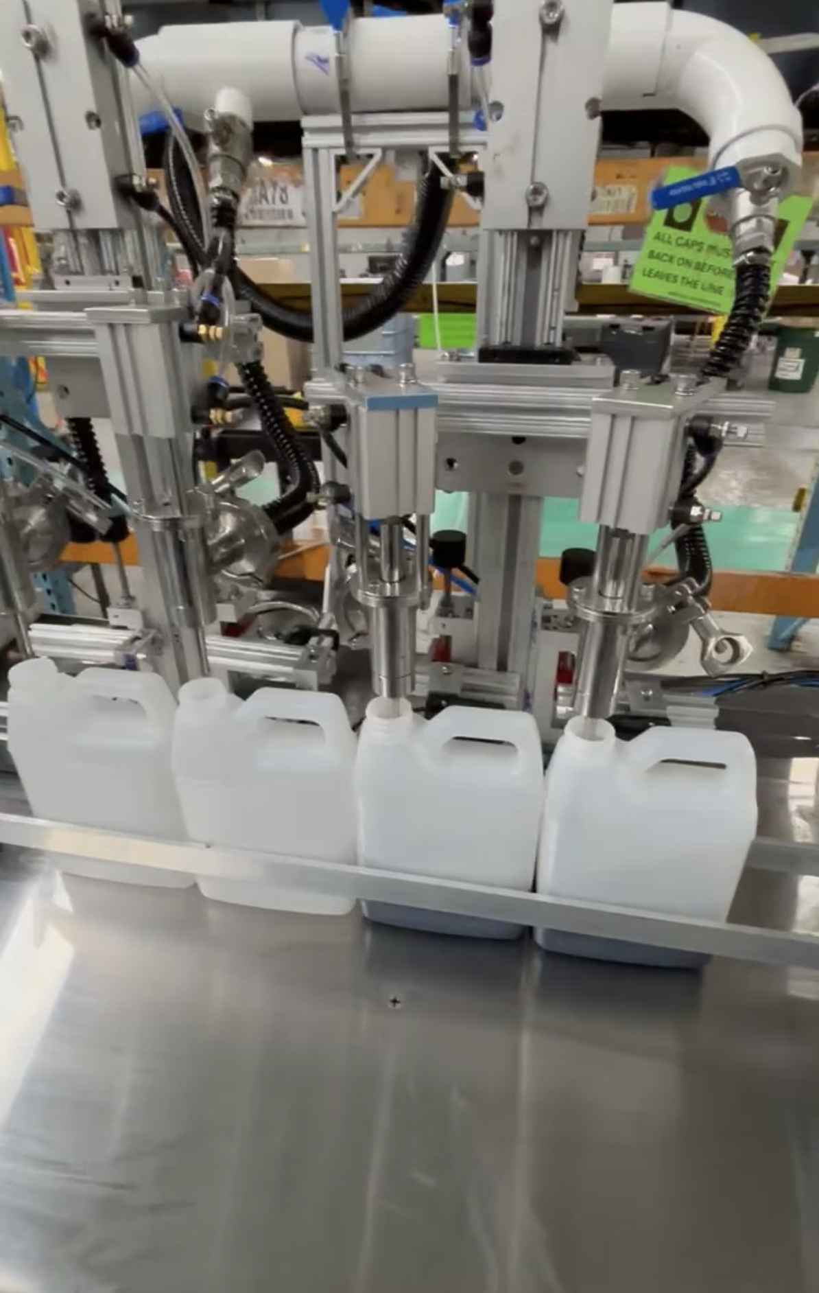 A liquid filling production line is in operation, with machinery dispensing fluid into large white containers.