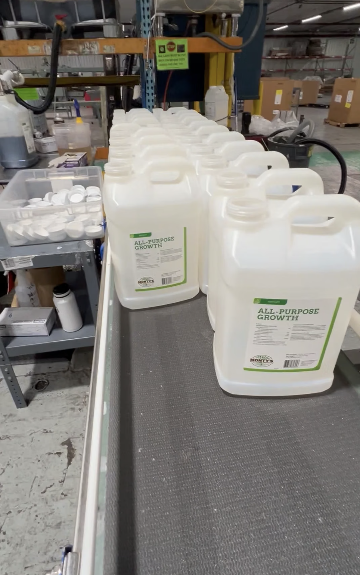 Several white plastic jugs are lined up on a conveyor belt in an industrial setting.
